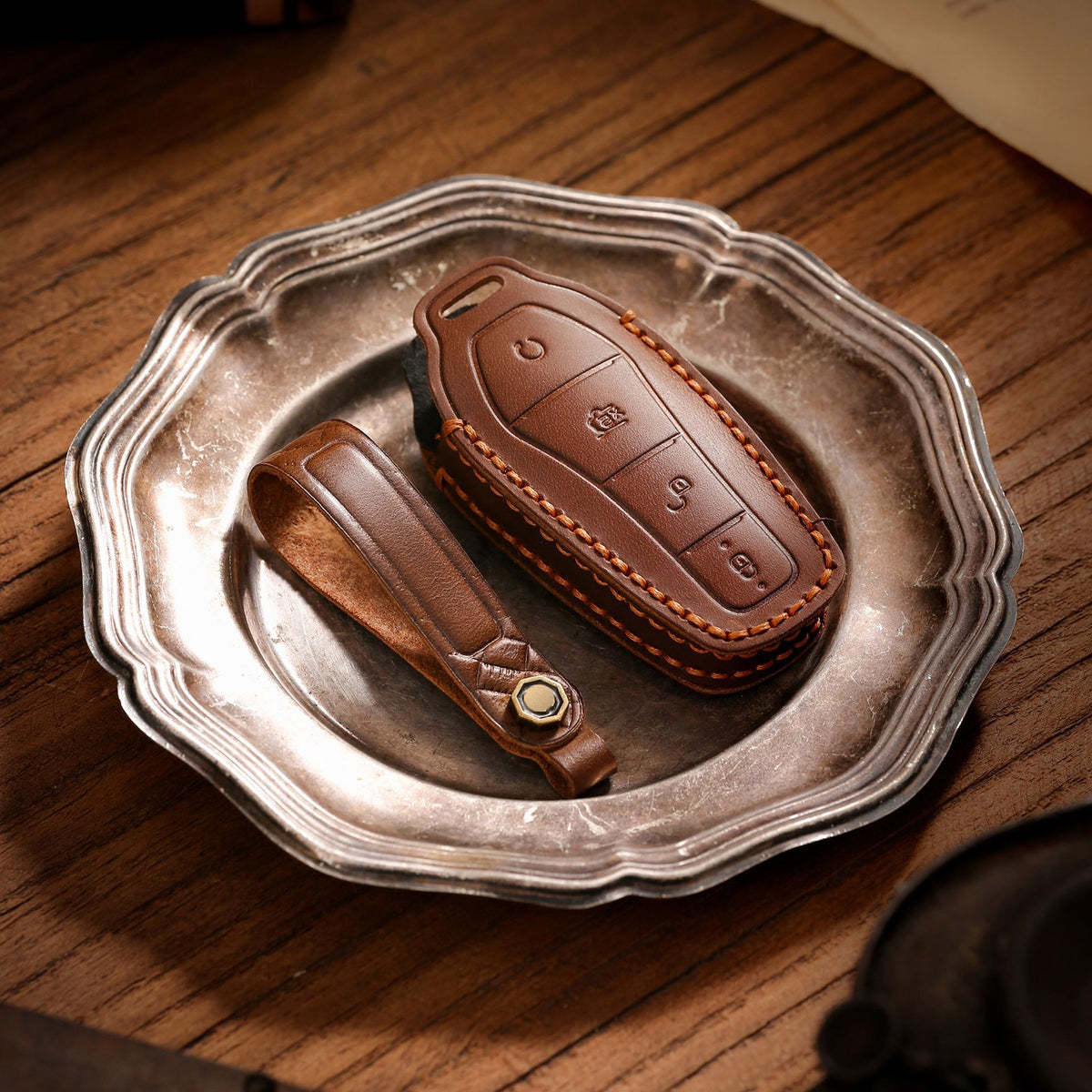 Brown leather key pouch and strap on a pewter plate